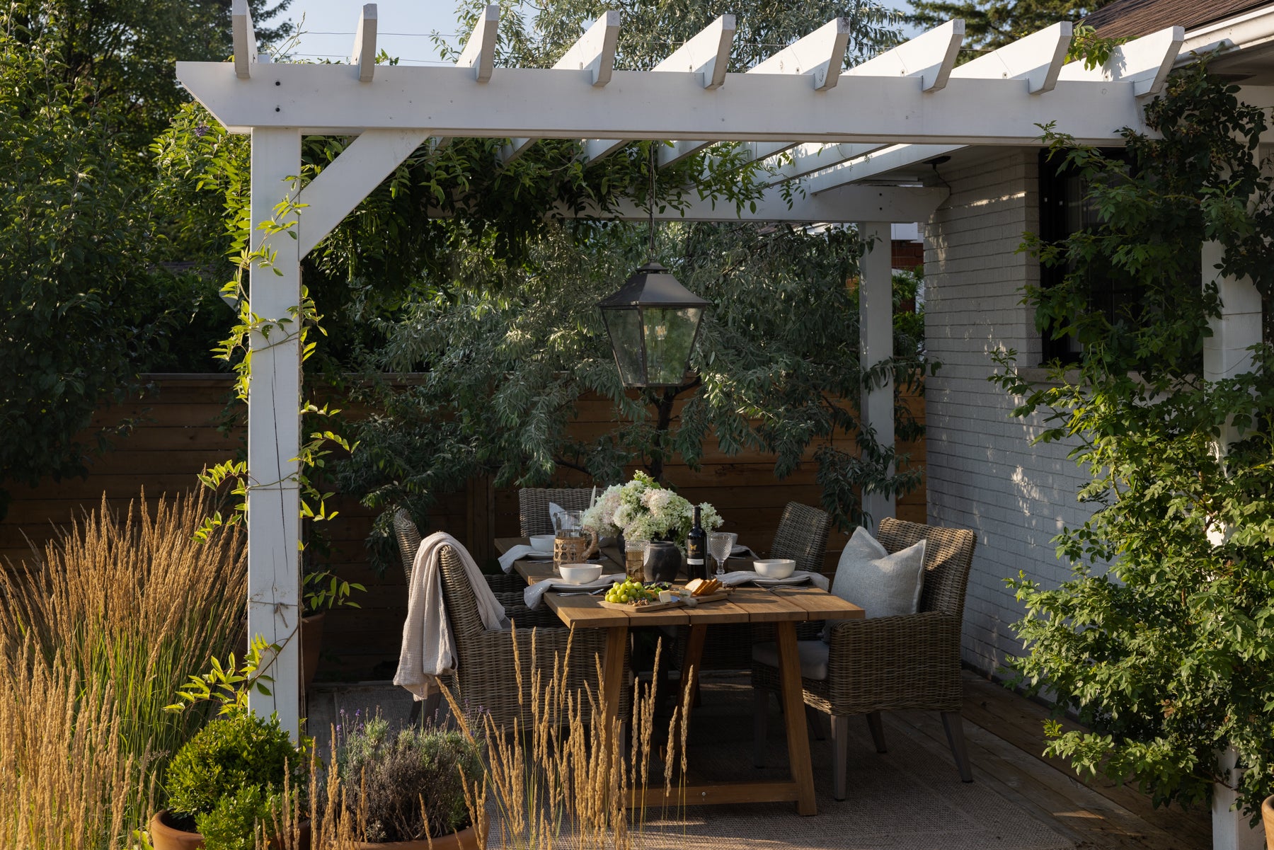 An outdoor table spread on a teak table under a white pergola.